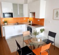 Eine Küche in einem Einzimmerapartment mit weißer Küchenzeile, orangefarbenen Fliesen und einem runden Tisch mit Holzdekor.