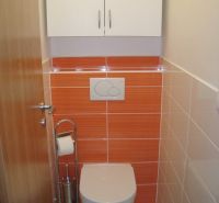 Toilette mit orangefarbenen Fliesen und weißem Schrank, Einzimmerwohnung.