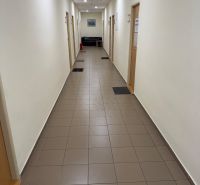 Ein enger Flur in einem Büro mit Fliesen, Türen und einem Sofa am Ende.