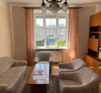 Wohnzimmer in einer Zweizimmerwohnung mit Sofa, Sesseln, Fernseher und Möbeln.