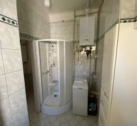 Badezimmer mit einer in der Ecke platzierten Duschkabine und einer Waschmaschine in einer 2-Zimmer-Wohnung.