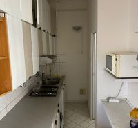Eine schmale Küche in einer Zweizimmerwohnung mit weißen Möbeln und Fliesen.