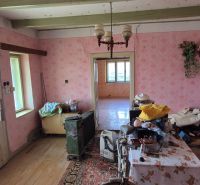 Ein Zimmer in einem Einfamilienhaus mit älteren Möbeln, rosa Tapeten und Holzboden.