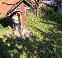 Der Garten des Einfamilienhauses in Dedinka mit Rasen, Gaszähler und einem Erdhaufen im Hintergrund.