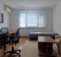 Wohnzimmer mit Sessel, Fernseher, Tisch und Holzboden in einer Zweizimmerwohnung.