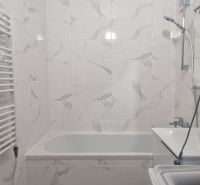 Badezimmer in einer 2-Zimmer-Wohnung mit Badewanne und Waschmaschine, gefliest mit hellen Fliesen.