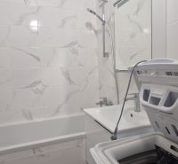 Badezimmer in einer 2-Zimmer-Wohnung mit Dusche, Badewanne und Waschmaschine, gefliest mit weißen Fliesen.