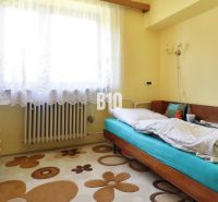 Ein Zimmer in einem Einfamilienhaus mit einem Einzelbett, einem Schrank und einem Fenster mit weißen Vorhängen.