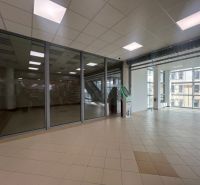 Verkaufslokale mit Glasfronten und Fliesenboden sowie einem Geldautomaten, Innenraum mit großen Fenstern.