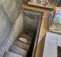 Betontreppen in der Hütte, die in den Keller führen, umgeben von gelagerten Gegenständen.