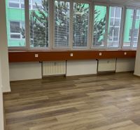 Büros mit großen Fenstern, Boden mit Holzdekor, helle Wände und abgehängte Decke.