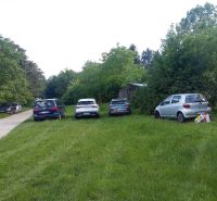 Autos parken auf dem Gras neben der Straße zwischen den Bäumen im Bereich Karloveská, Bratislava - Karlova Ves.