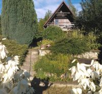 Eine Hütte im Garten mit Holzelementen, umgeben von Grün und weißen Blumen.