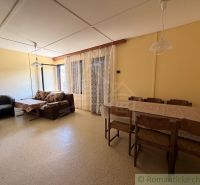 Das Innere der Hütte mit Esstisch, Sessel und Sofa neben Fenstern mit Spitze.