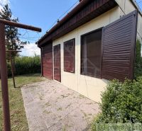 Eine Hütte in Nové Zámky mit geschlossenen hölzernen Fensterläden und umgebendem Grün im Garten.