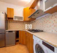 Küche mit gefliester Wand, Geräten und Holzboden in einer Zweizimmerwohnung.