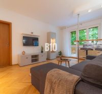 Wohnzimmer in einer 2-Zimmer-Wohnung mit Holzboden und Sitzgelegenheit am Fenster.