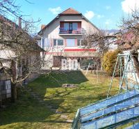Ein Einfamilienhaus in Turany mit Rasen, Bäumen und einem Gewächshaus im Garten.