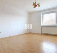 Ein geräumiges Zimmer mit weißen Wänden in einem Einfamilienhaus und einem Boden in Holzoptik.