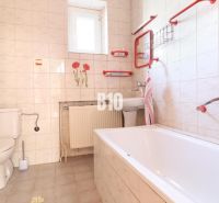 Badezimmer im Einfamilienhaus: Badewanne, Waschbecken, Toilette, weiße Fliesen mit roten Elementen.