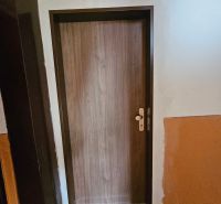 Eingangstür mit Holzdekor und schwarzer Fußmatte, Einzimmerwohnung.
