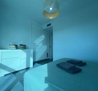 Ferienwohnung mit einem hellen Zimmer, Bett, Kommode und Loggia in blauen Tönen.