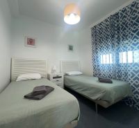 Ferienwohnung mit zwei Einzelbetten, gemusterten Vorhängen und einem Tisch mit Lampe.