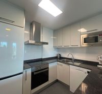 Küche in einer Ferienwohnung mit weißen Schränken, Geräten und schwarzer Arbeitsplatte.