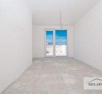 Ein leerer Raum mit Betonboden und Balkontüren in einer 3-Zimmer-Wohnung.