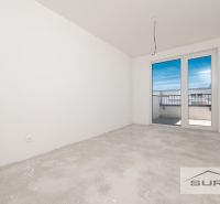 Ein leeres Zimmer in einer 3-Zimmer-Wohnung mit Zugang zum Balkon und unfertigem Boden.