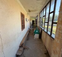 Ein schmaler Gang auf der Veranda in einem Einfamilienhaus mit alten Fenstern und rissigen Wänden.