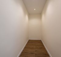 Ein enger Flur in einem Einfamilienhaus mit weißen Wänden und einem Boden in Holzoptik.
