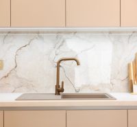 Küchenzeile mit goldenem Wasserhahn und Marmorverkleidung in einem Einfamilienhaus.