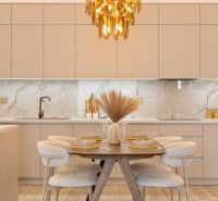 Küchenbereich mit Esstisch, beige Schränke, Boden mit Holzdekor, Leuchte.