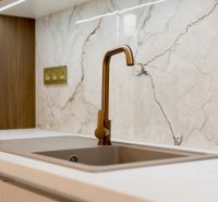Küchenarmatur und Arbeitsplatte im Einfamilienhaus mit Marmor-Dekor an der Wand.