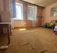 Ein Zimmer in einer 2-Zimmer-Wohnung mit Teppich, offenem Fenster und einfacher Einrichtung.