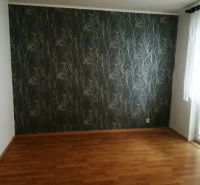 Ein Zimmer in einer 3-Zimmer-Wohnung mit einem Holzboden und gemusterten Tapeten.