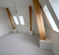 Dachgeschosszimmer mit weißer Wand und Holzbalken in einer 2-Zimmer-Wohnung.