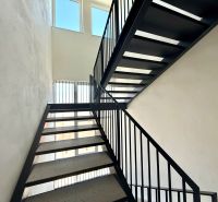 Eine Treppe in einer 2-Zimmer-Wohnung mit einem schwarzen Geländer und großen Fenstern.