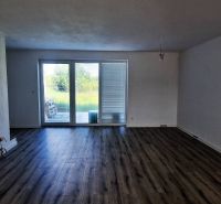 Ein Zimmer in einem Einfamilienhaus, große Fenster, weiße Wände, Holzboden.