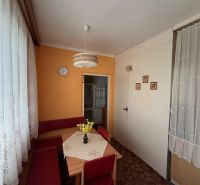 Küche in einer 2-Zimmer-Wohnung mit orangefarbener Wand, Teppich und Spitzenvorhängen.