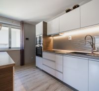 Eine Küche in einem Einfamilienhaus mit weißen Schränken, einem Boden in Holzoptik und einem Fenster.