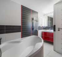 Badezimmer in einem Einfamilienhaus mit Badewanne, rotem Schrank und silbernem Heizkörper.