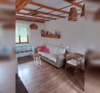 Ein Interieur in einem Einfamilienhaus mit einem Boden in Holzoptik, einem Rattansessel und einem Sofa.