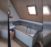 Badezimmer mit Badewanne und schräger Decke, Holzelemente, Mosaikfliesen, Fenster.