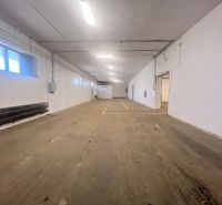 Innenraum eines Lagers mit Betonboden und weißen Wänden, Leuchtstoffbeleuchtung.