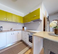 Küche mit weißen und gelben Schränken, Mikrowelle und dekorativen Blumen in einer 3-Zimmer-Wohnung.