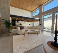 Wohnbereich in einem Einfamilienhaus mit Treppe, Sofa und großen Fenstern zur Terrasse.
