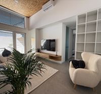 Wohnzimmer in einem Einfamilienhaus mit einem cremefarbenen Sessel und einem Fernseher, Boden mit Holzdekor.