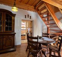 Innenraum einer Hütte mit hölzerner Treppe, Esstisch und rustikalem Schrank.